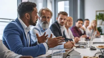 Image of a board meeting with several individuals listening and one person talking